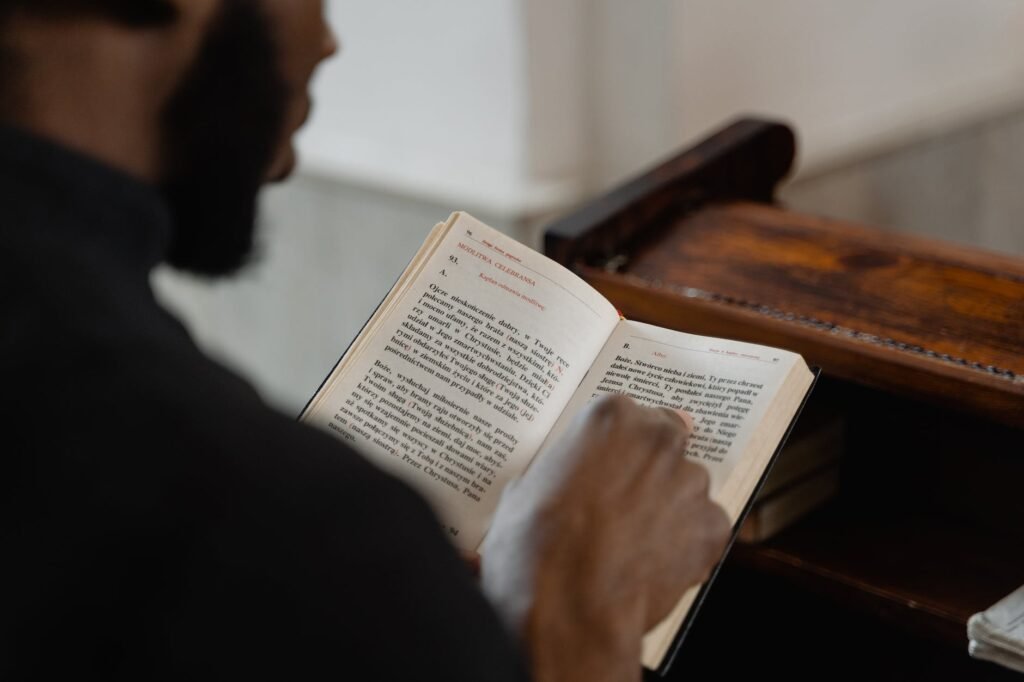 vyras juodu apsiaustu skaitantis šventąją Bibliją
